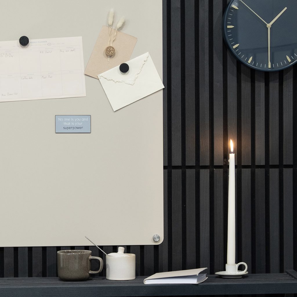 Immagine mostra prodotti WoodUpp: pannello a doghe in legno nero verticale (parete fonoassorbente), lavagna magnetica crema con angoli arrotondati e viti di fissaggio metalliche, insieme a magneti WoodUpp (tondi neri e targhetta rettangolare azzurra con frase) per appunti, decorativa e minimalista.