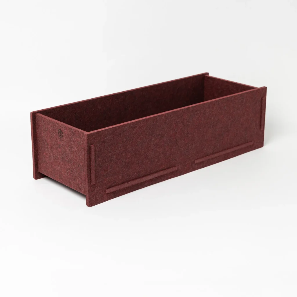 Immagine di prodotto WoodUpp: fioriera rettangolare in feltro bordeaux, lunga e bassa, con pareti spesse, angoli ad incastro e scanalature laterali per montaggio. Interno vuoto, superficie morbida e texture tessuta; piccolo logo WoodUpp inciso su un lato, design minimal e modulare.