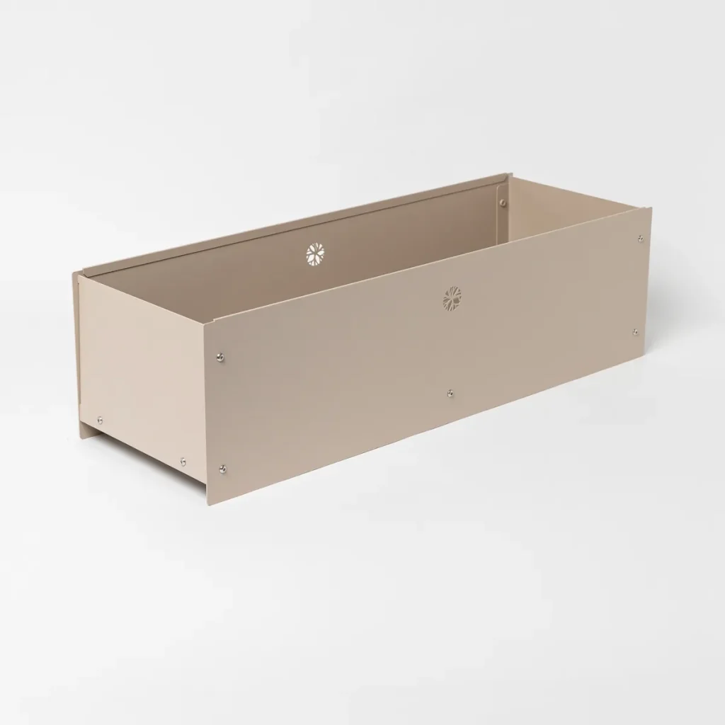 Fioriera rettangolare WoodUpp in metallo color sabbia, con pannelli avvitati e finitura opaca; interno vuoto, bordo rinforzato e piccoli fori decorativi a forma di fiore per drenaggio; design basso e lineare ideale per balconi e terrazzi, resistente alle intemperie e facile da montare; viti inox visibili.