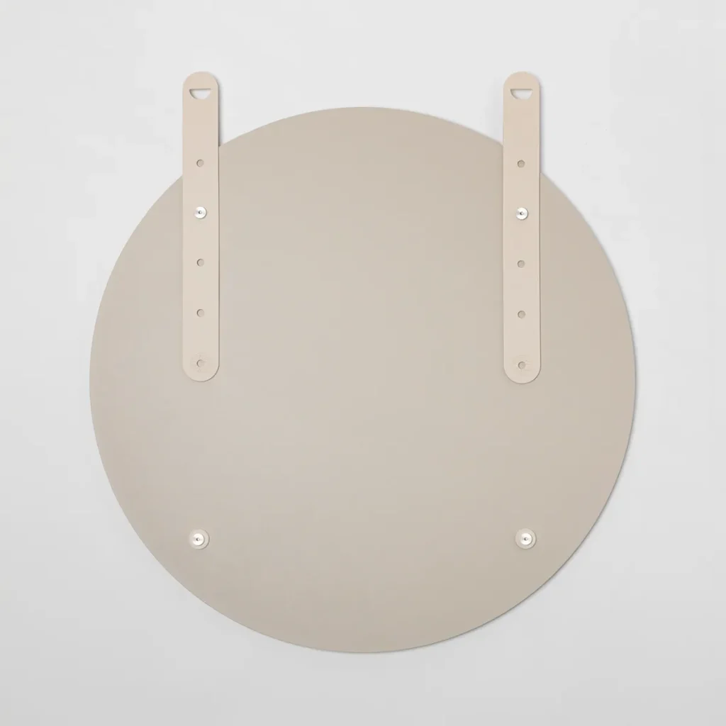 Retro di uno specchio rotondo WoodUpp color sabbia: disco circolare opaco con due cinghie in pelle beige regolabili fissate da viti metalliche e due placchette magnetiche inferiori. Design minimalista, pulito ed elegante, pensato per l’appensione a parete con supporti robusti e di alta qualità.