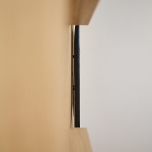 Vista laterale di un sistema WoodUpp: sottile staffa di montaggio nera a profilo piatto fissata alla parete, incassata tra due pannelli/ripiani in legno chiaro (rovere). Immagine minimalista ed elegante che mostra il fissaggio slim e la finitura naturale dei prodotti WoodUpp modulari.
