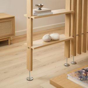 Separé modulare WoodUpp in rovere chiaro: pannelli verticali a listelli con ripiani integrati che fungono da mensole sottili, fissaggi a vite e piedini regolabili in metallo; l'immagine mostra due ripiani con libri, scodelle e gomitoli, stile minimal e finitura naturale.