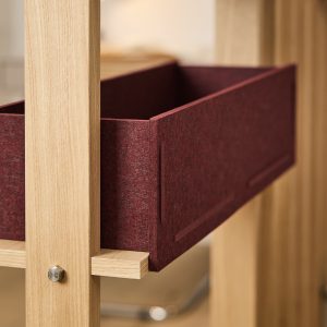Immagine WoodUpp: primo piano di una struttura in rovere chiaro con scaffale e supporti, che ospita un cassetto estraibile in feltro bordeaux di WoodUpp; dettaglio del legno naturale, viti metalliche e la superficie morbida e fitta del contenitore in feltro.