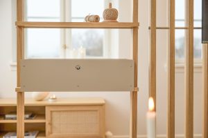 Struttura divisoria WoodUpp in rovere chiaro con stecche verticali e mensola superiore, affiancata da un pannello metallico beige WoodUpp montato al centro. In scena matasse di spago sulla mensola, candele accese e un mobile basso in legno chiaro sullo sfondo.