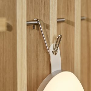 Primo piano di un pannello modulare in rovere WoodUpp con listelli verticali chiari, dotato di una barra orizzontale e di un gancio appendiabiti in acciaio inox WoodUpp che regge una lampada tonda dal supporto bianco. Texture del legno e finiture metalliche nitide.