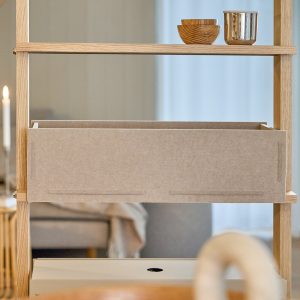 Scaffale in rovere WoodUpp con ripiani sottili, contenitore scatola portaoggetti in tessuto beige WoodUpp inserito al centro, in alto due ciotole di legno impilate e un vasetto metallico. Con finitura chiara e giunzioni a incastro, pratico vano organizzativo, vista laterale ravvicinata.