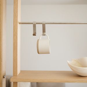 Scaffale in legno WoodUpp con barra metallica: due ganci in acciaio WoodUpp appesi alla barra, uno regge una tazza smaltata color crema. Sulla mensola sottostante una ciotola decorativa crema. Composizione minimalista, finiture naturali e acciaio satinato. Dal design semplice e lineare, ogni elemento è curato nei dettagli.