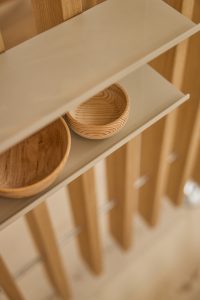 Immagine WoodUpp: prodotti visibili WoodUpp sono mensole sottili color sabbia appoggiate su parete a listelli verticali in legno naturale; due ciotole in legno curvato riposano sulla mensola, venature evidenti e finitura liscia, atmosfera minimal e calda, elegante, con finiture curate e linee pulite.